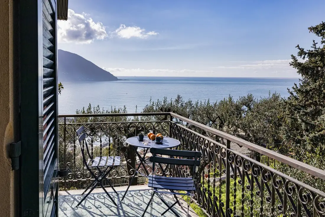 A small balcony with a table and seating overlooks the sea.