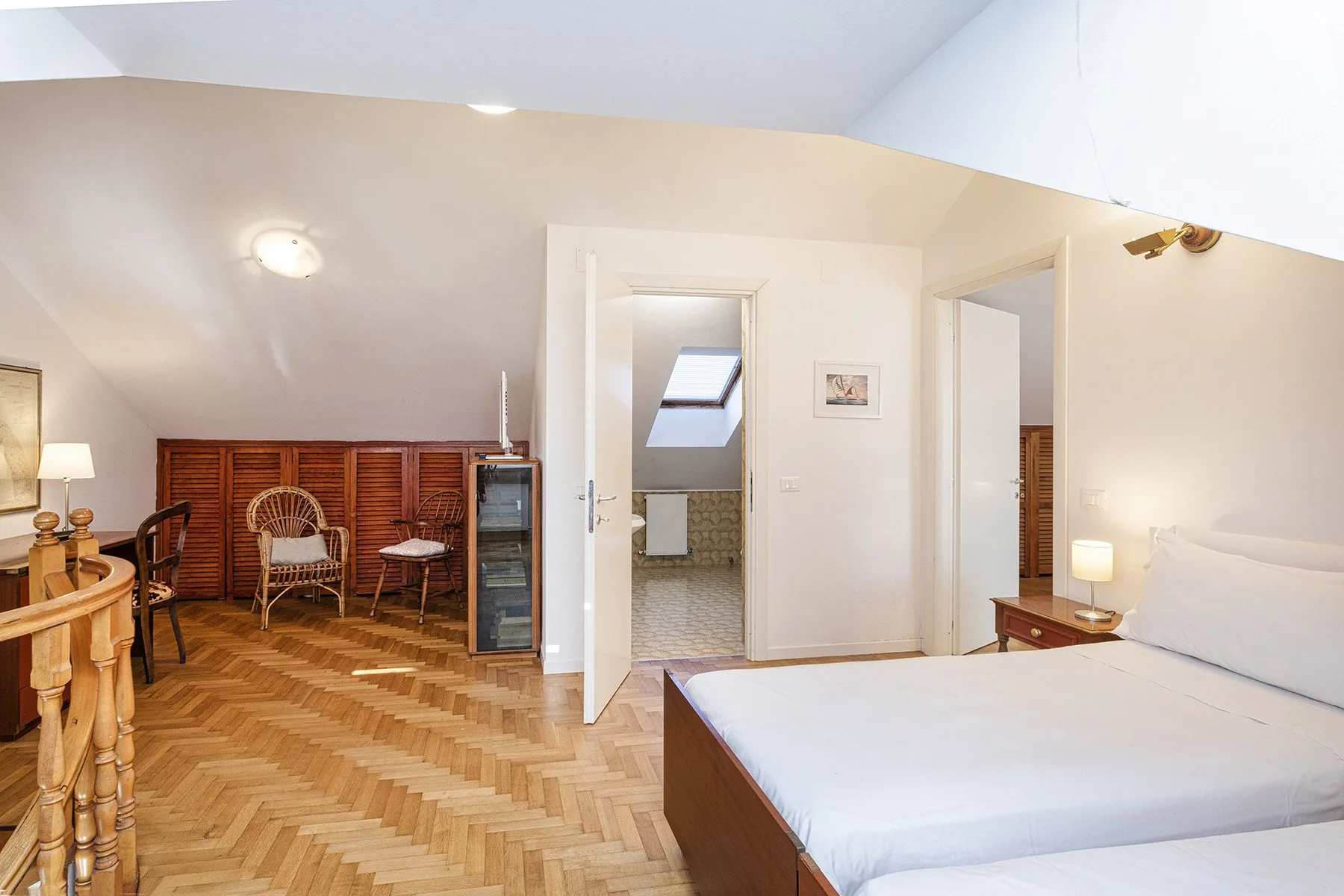 A bedroom with a bed, parquet flooring, and an open doorway to a bathroom.