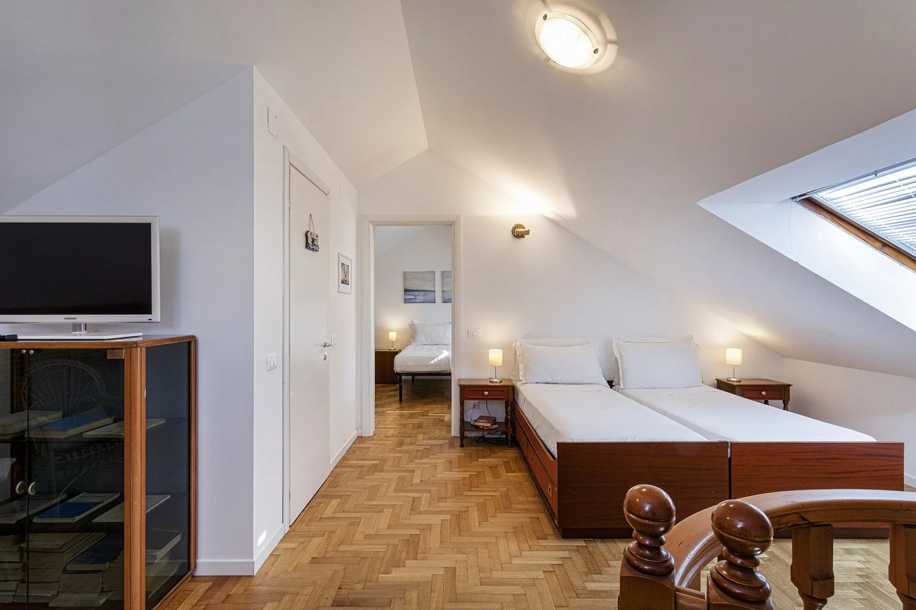 A bright attic bedroom with two beds and a television.