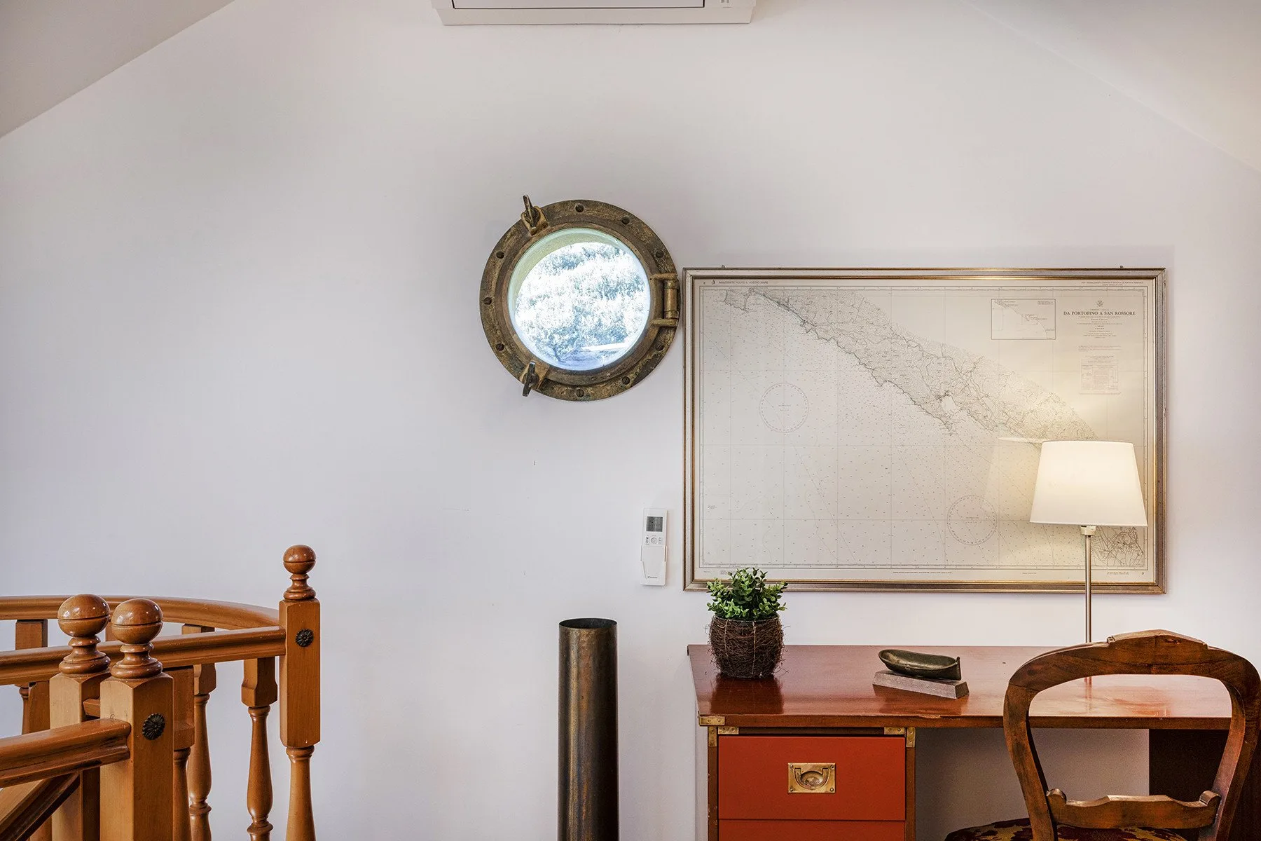 A small study area with a desk, wall map, and round window.