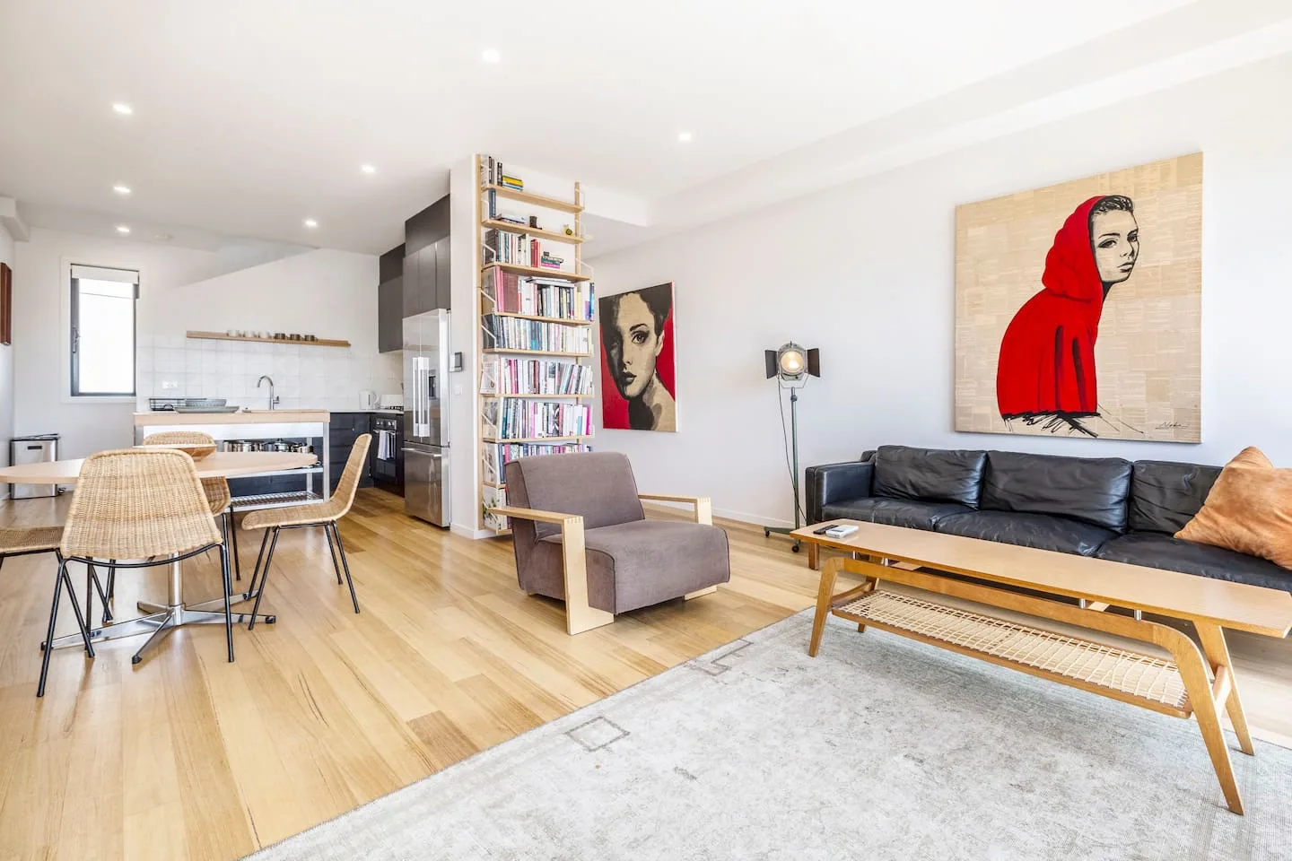 Una sala de estar y cocina de concepto abierto, con una estantería y retratos coloridos.