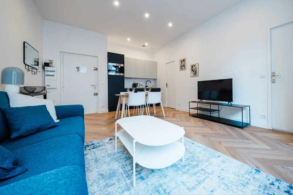 A bright living room with blue seating, a white coffee table, and a dining area.