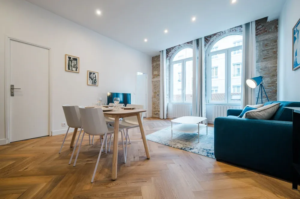 A bright living and dining area with a table beside tall arched windows.