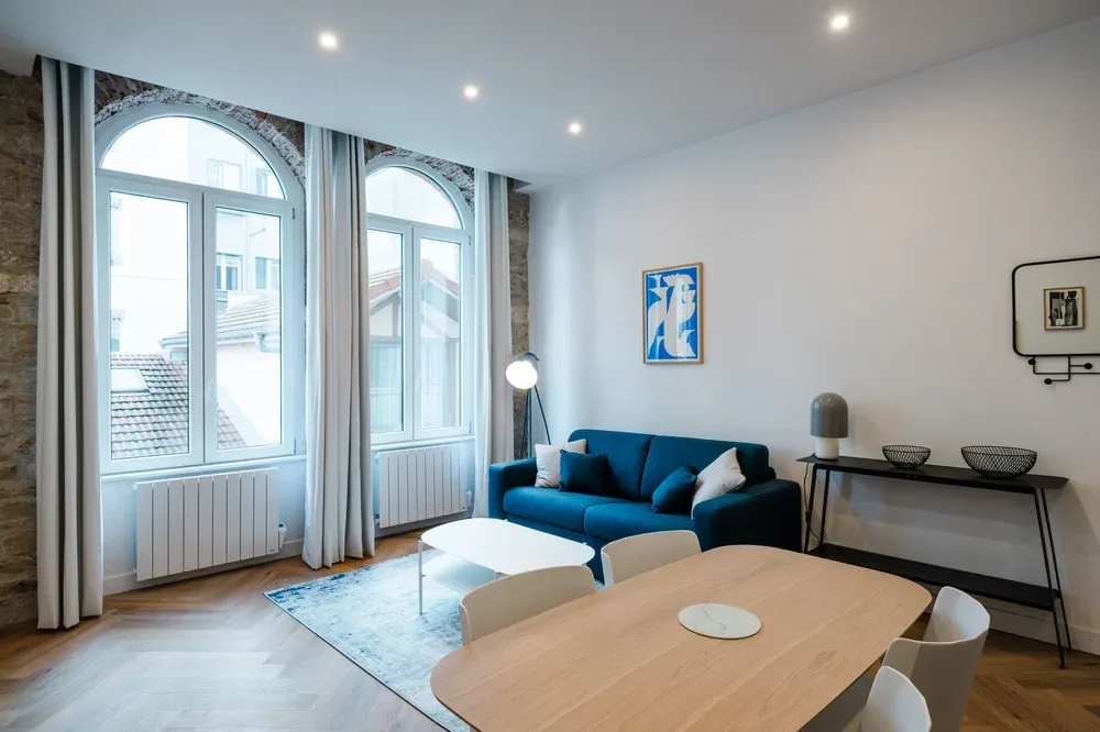 A bright living room with blue seating, arched windows, and a wooden dining table.
