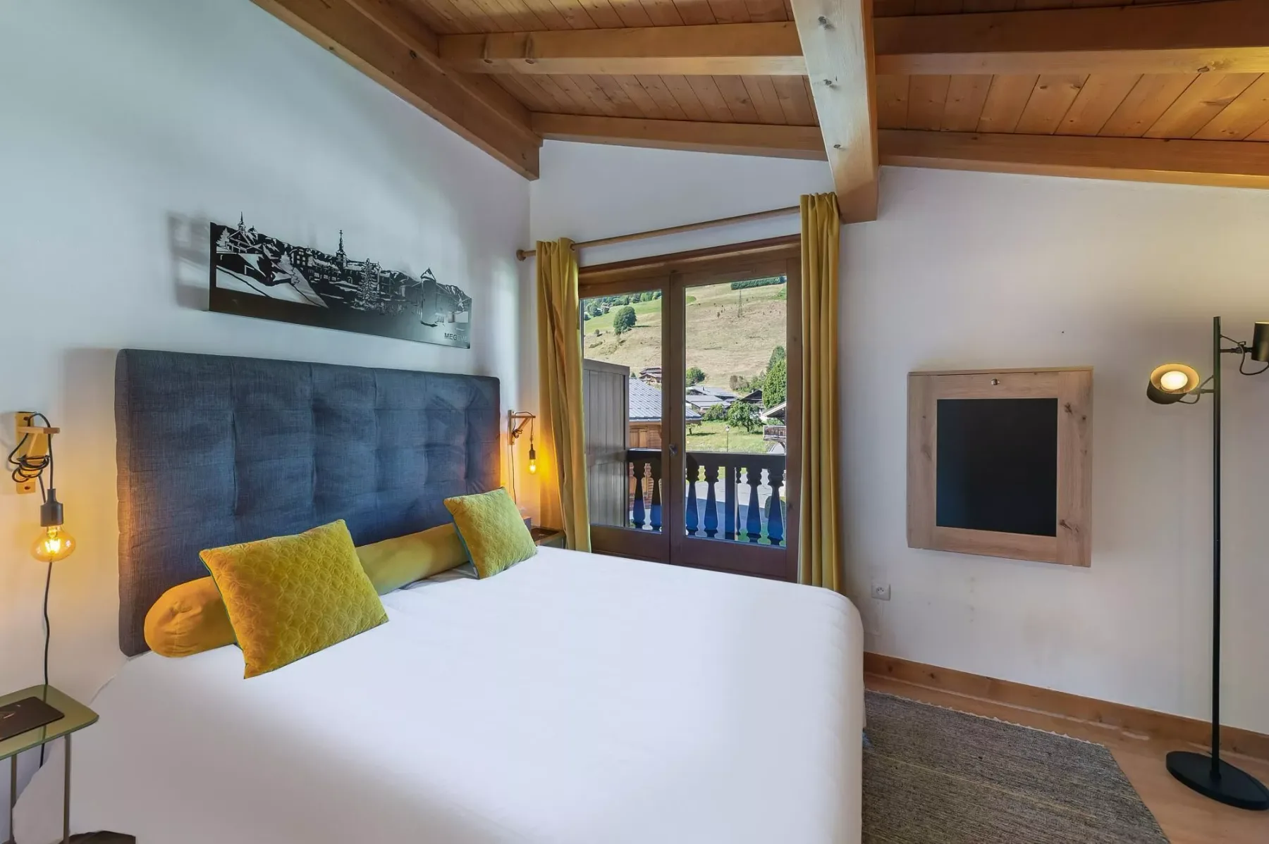 A bedroom with a bed beneath exposed wooden ceiling beams and a balcony window.