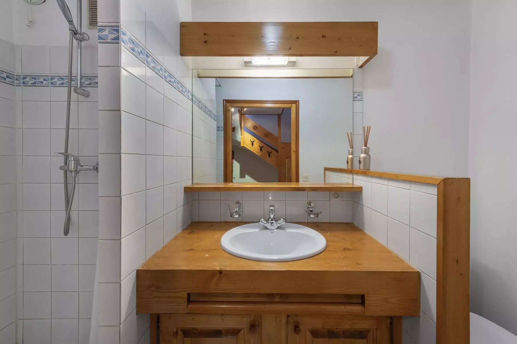 A tiled bathroom with a wooden vanity and a sink beneath a mirror.