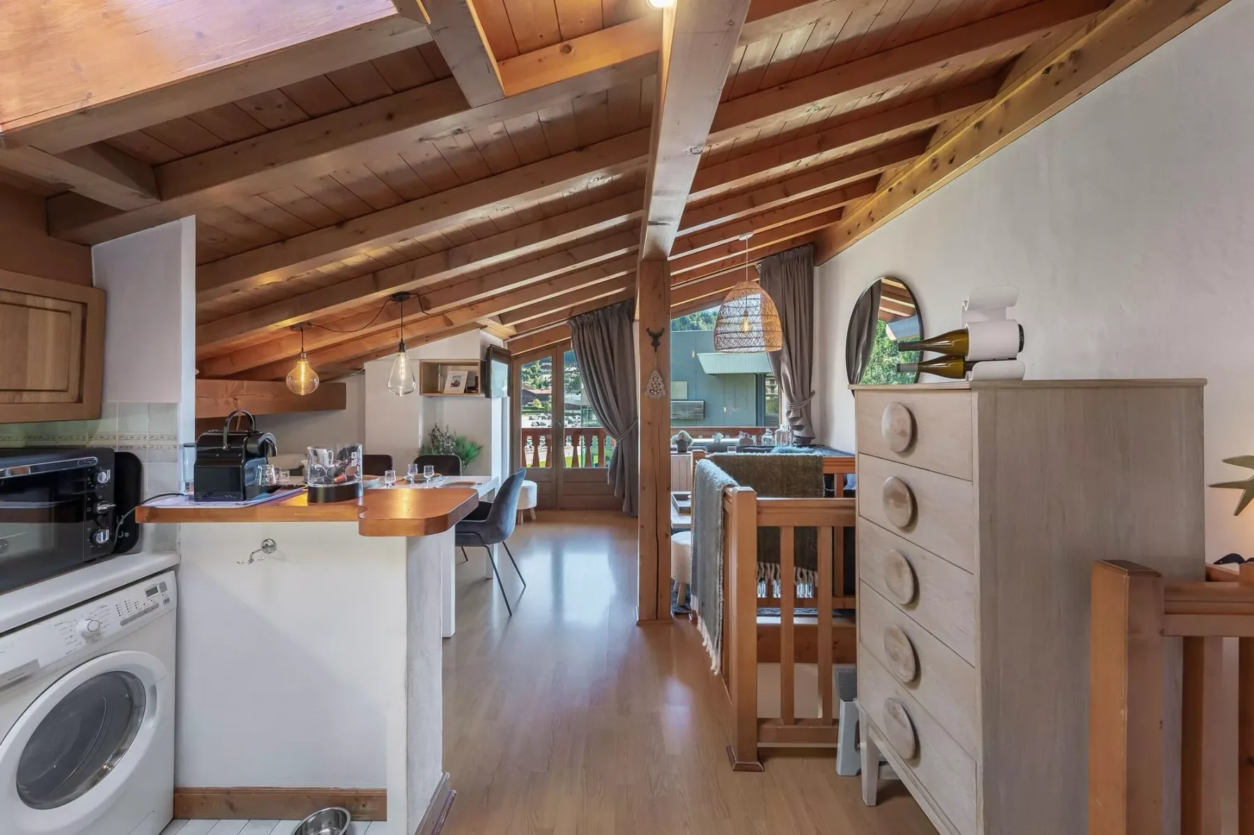 A compact open-plan room with a kitchen, dining area, and sloped wooden ceiling.