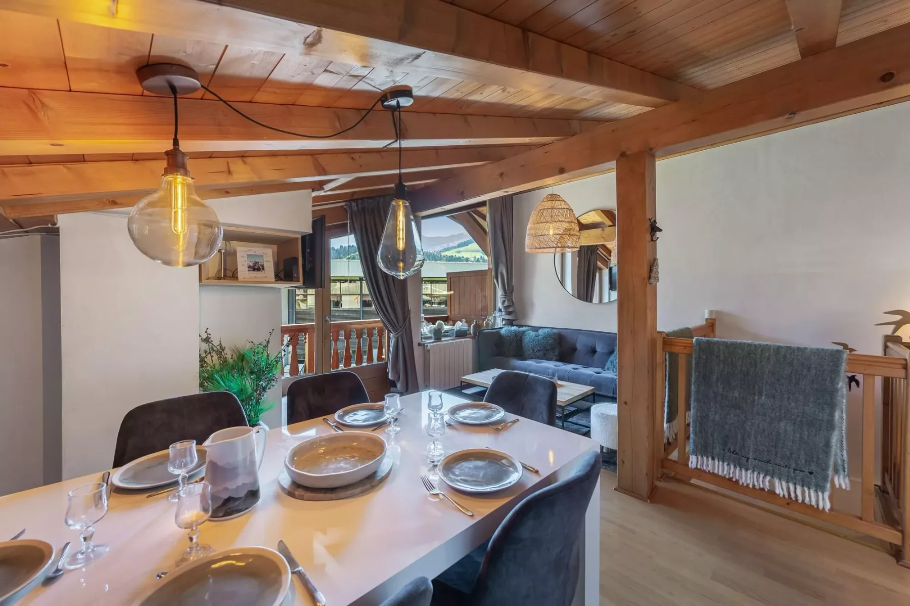 Un comedor se abre a una sala con un sofá y grandes ventanas.