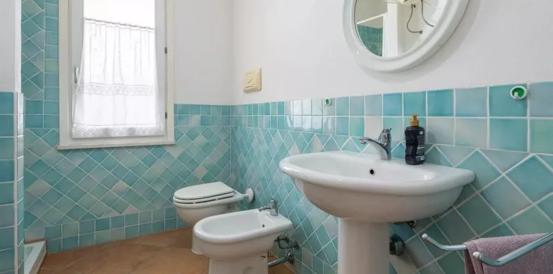 Un baño con azulejos, lavabo, inodoro, bidé y ventana.