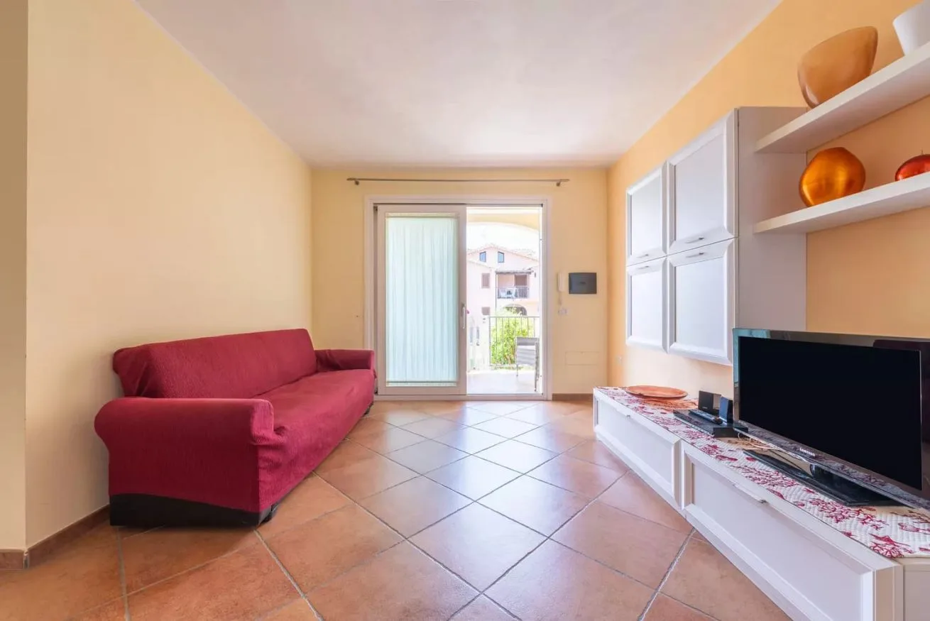 Una sala de estar con asientos rojos, un mueble para televisor y una puerta acristalada al balcón.