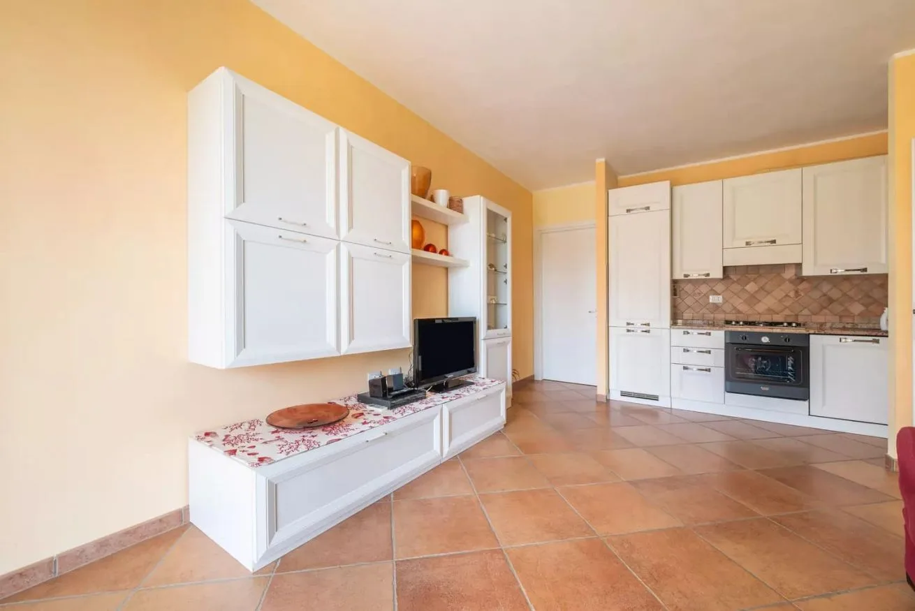 Una cocina y sala de estar integradas con gabinetes blancos y un televisor.