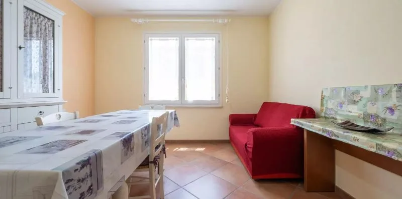 A dining area with a table beside a red sofa and a window.