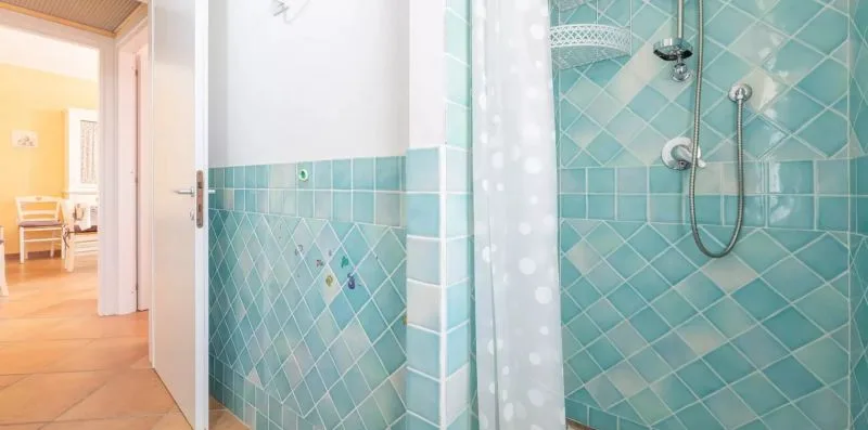 Un baño alicatado con ducha y una puerta abierta a una habitación contigua.