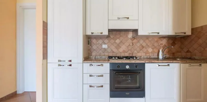 Una cocina luminosa con armarios blancos, salpicadero de azulejos y horno integrado.