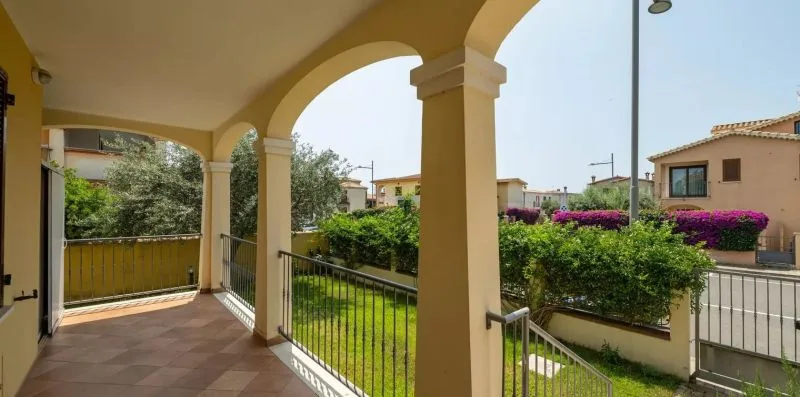Un pasillo exterior cubierto con arcos da a un jardín ajardinado.