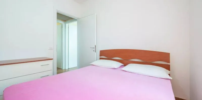 Un dormitorio con una cama cubierta con ropa de cama rosa y una cómoda blanca.