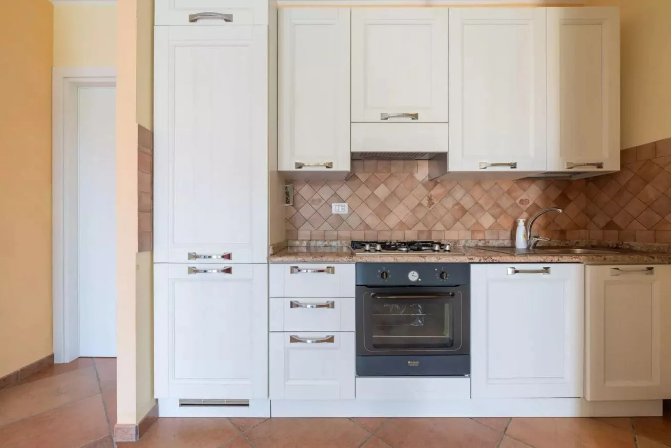 Una cocina equipada con armarios blancos, un horno y un salpicadero de azulejos.