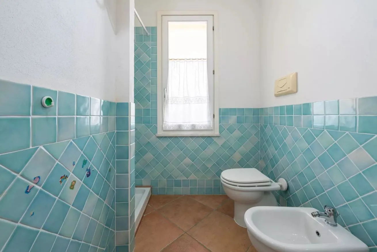 Un baño con paredes de azulejos turquesa, un inodoro y un lavabo.