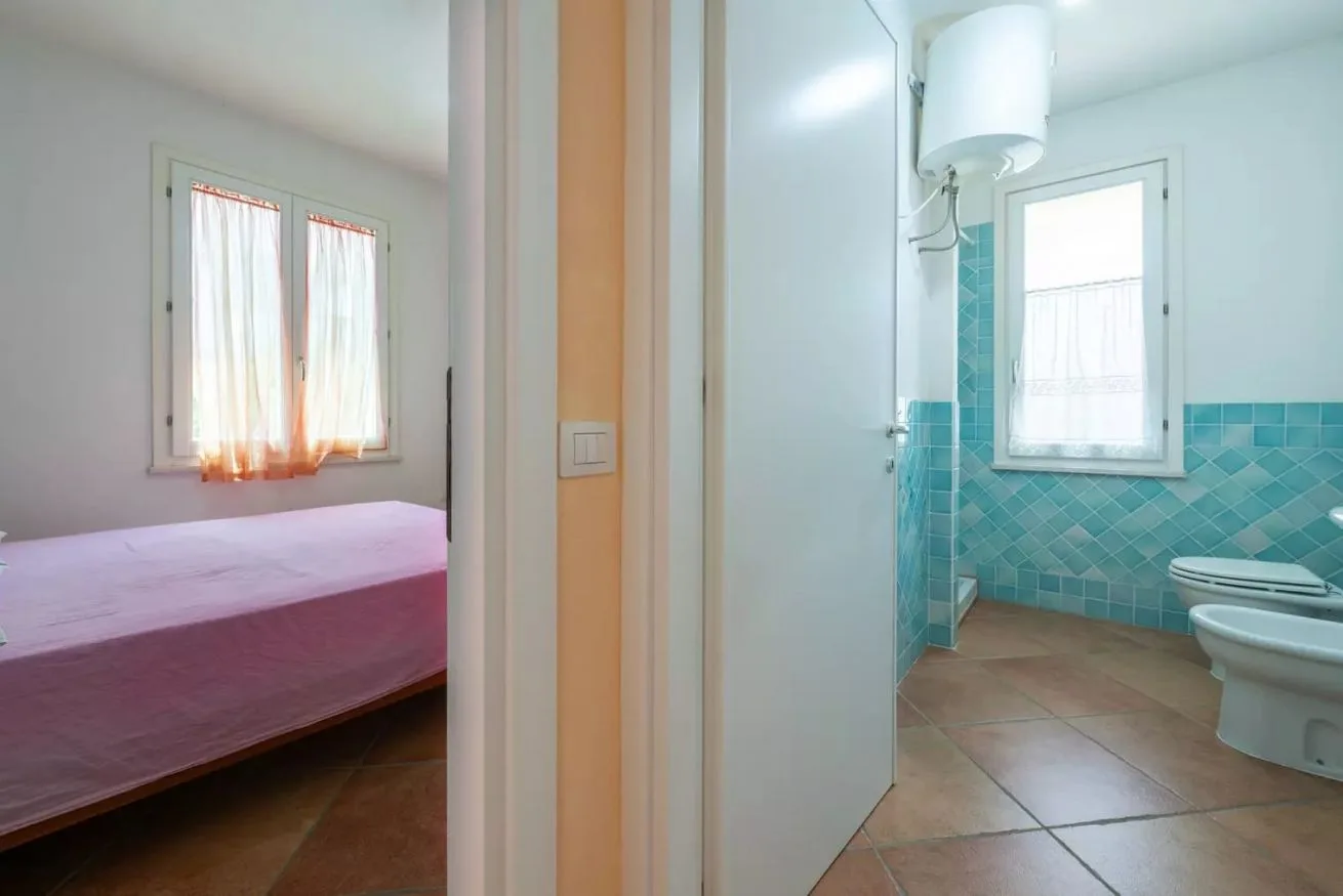 Se ve un dormitorio con una cama junto a un baño con paredes de azulejos turquesa.