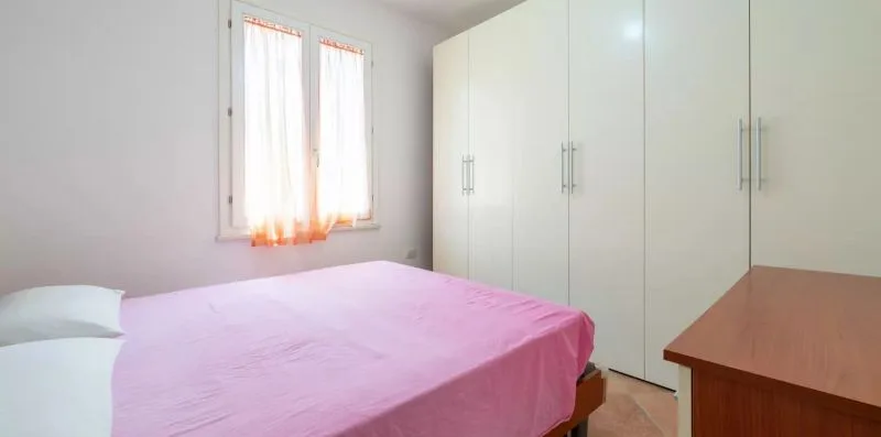 Un dormitorio con una cama cubierta con ropa de cama rosa y un armario blanco.
