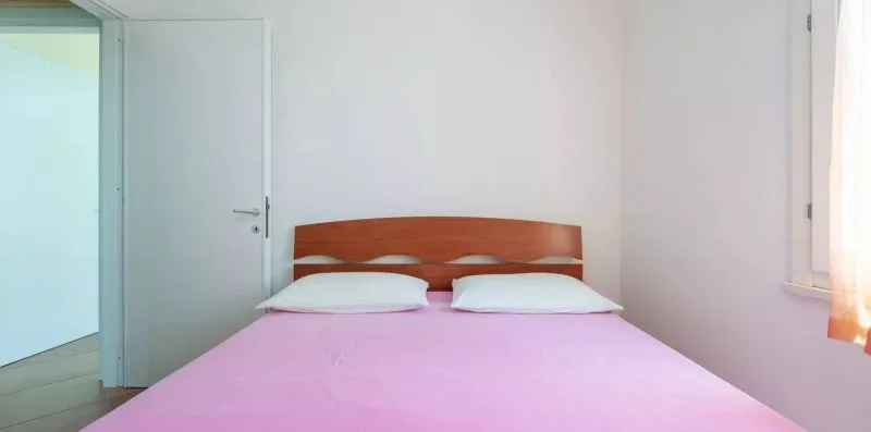 Un dormitorio con una cama cubierta con ropa de cama rosa y una ventana.