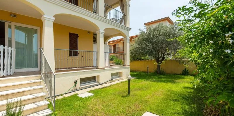 A sunny garden lawn borders a cream-colored building with arched balconies.