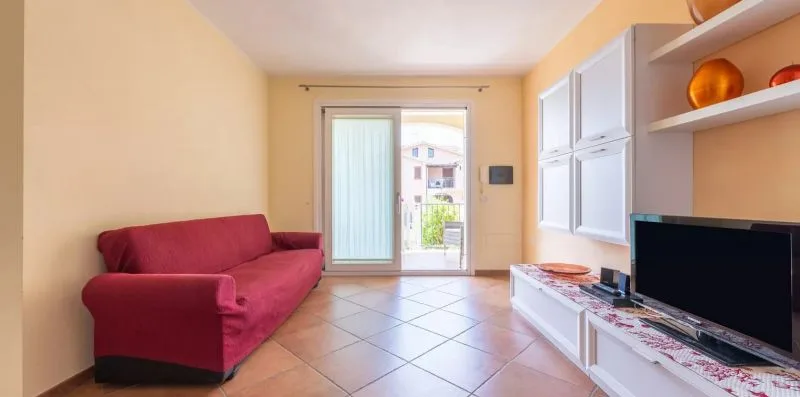 A living room with a red sofa, tiled floor, and television.