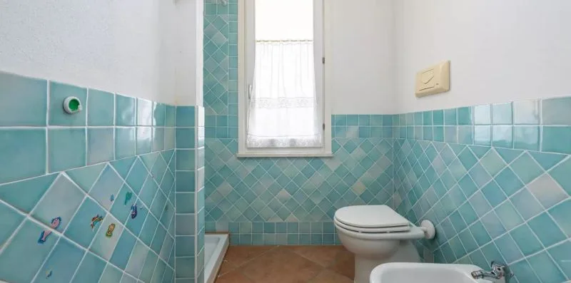Un baño alicatado con inodoro, bidé y una pequeña ventana con cortina.