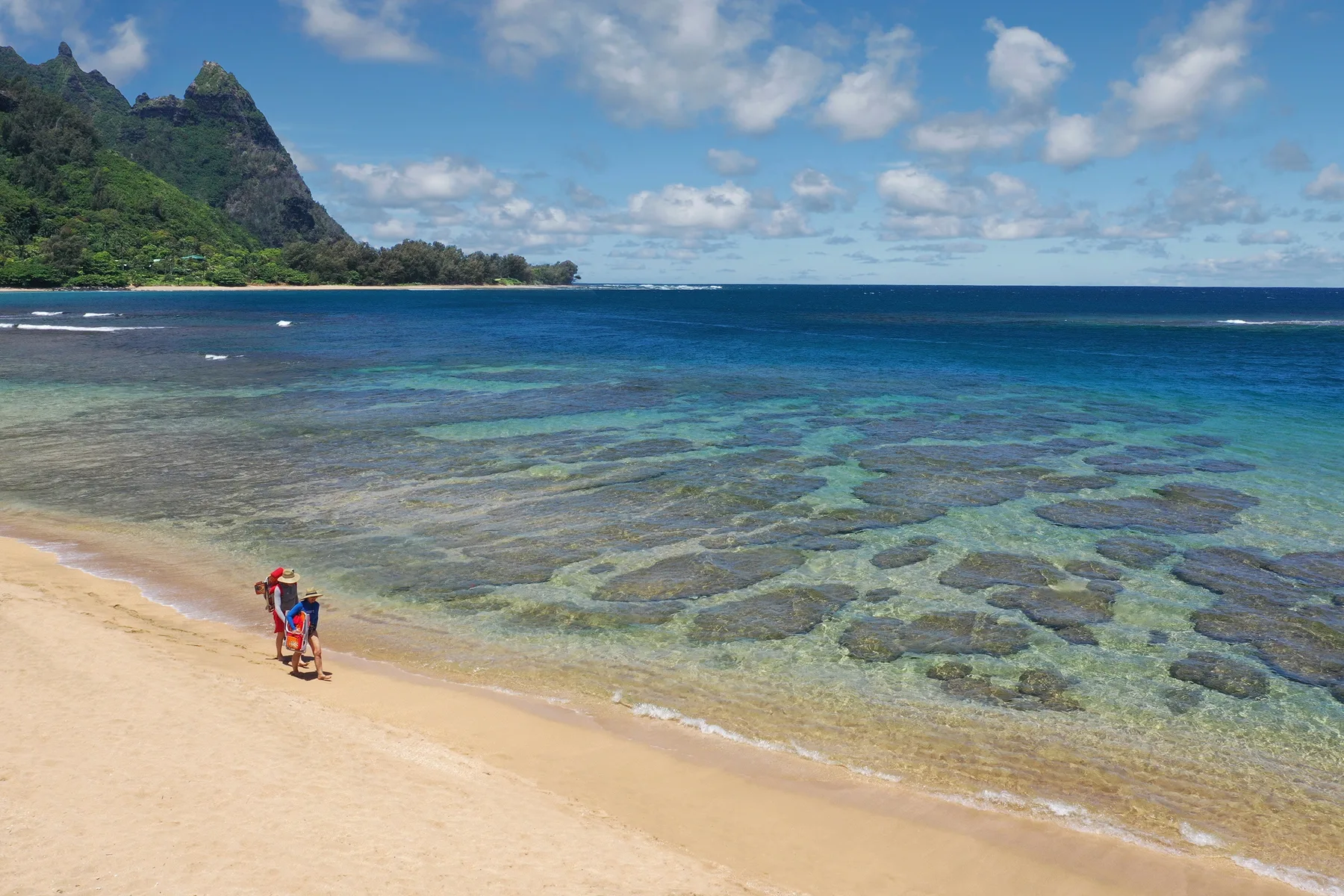 A sandy beach borders clear, shallow water with a green headland in the distance.