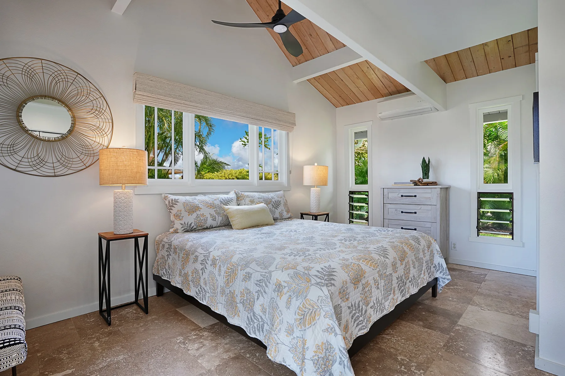 A bright bedroom with a large bed beneath a high, wood-paneled ceiling.