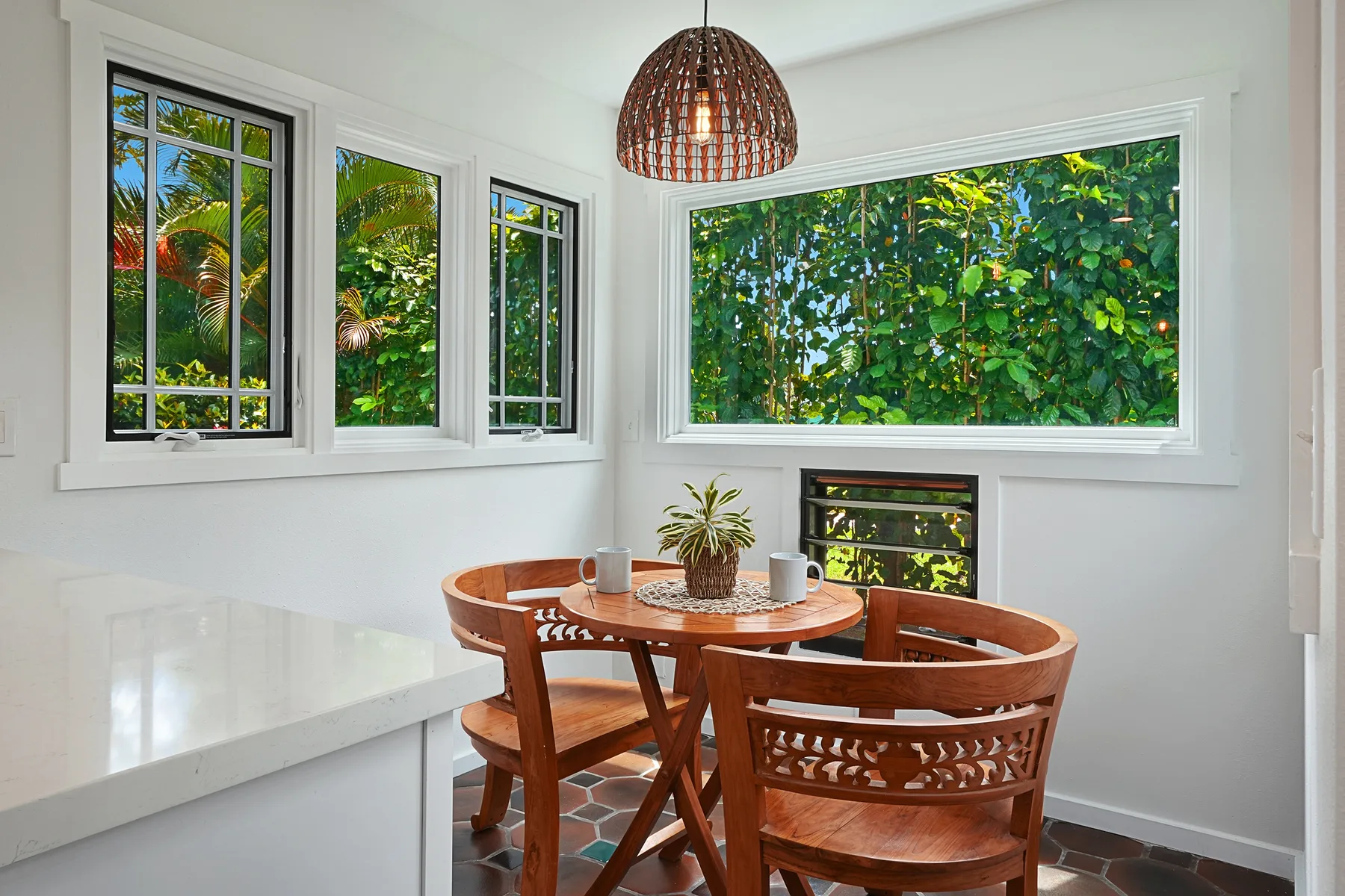 Un luminoso rincón de comedor con una mesa redonda de madera junto a grandes ventanas con vistas a la vegetación.