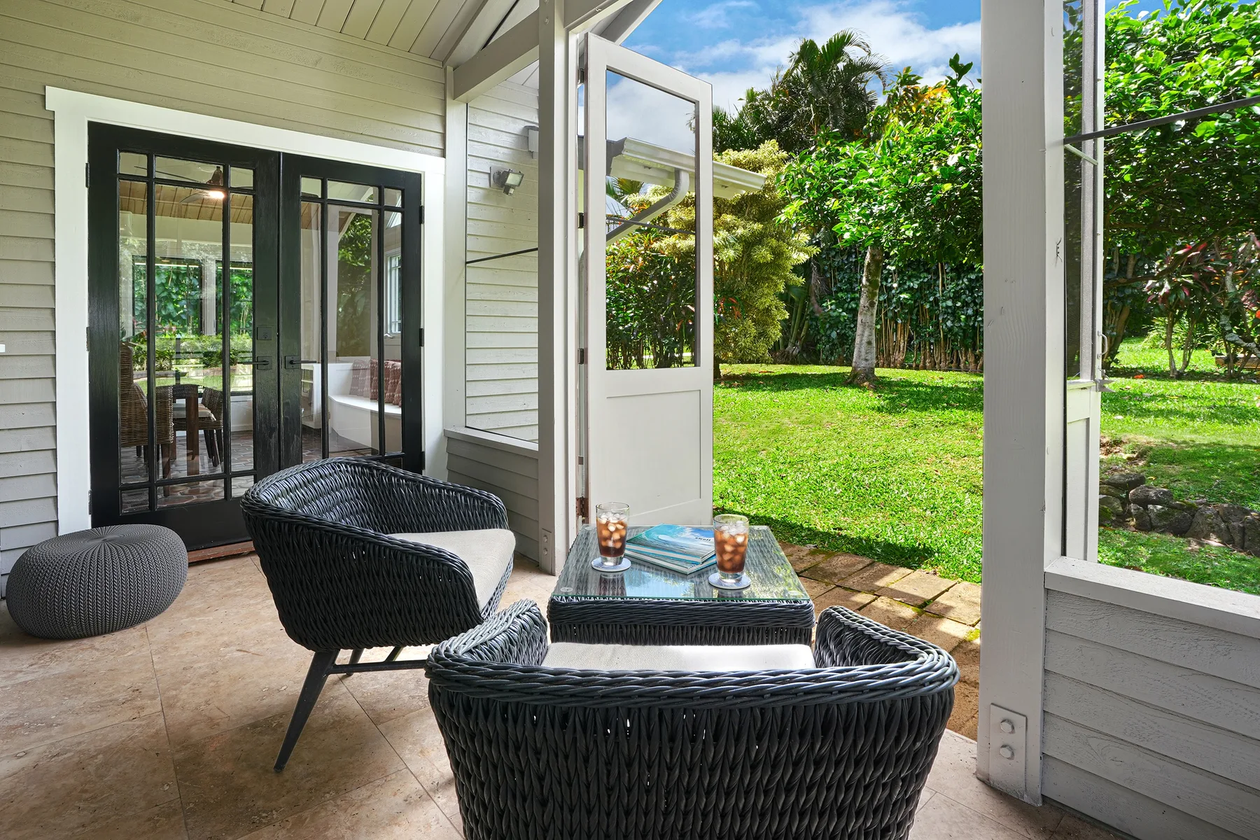 A covered patio with dark woven seating opens onto a green garden.