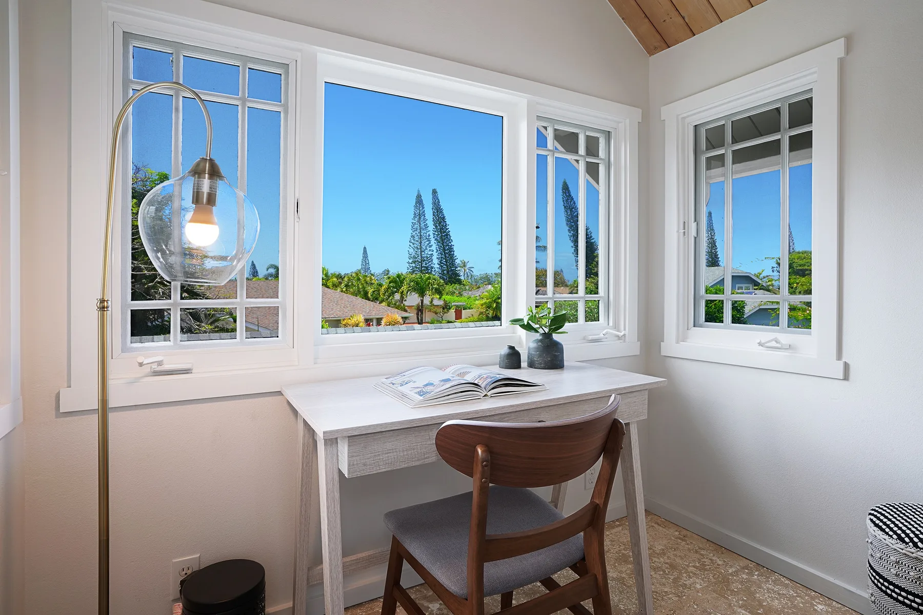 A small desk and chair sit beside several windows overlooking trees and rooftops.