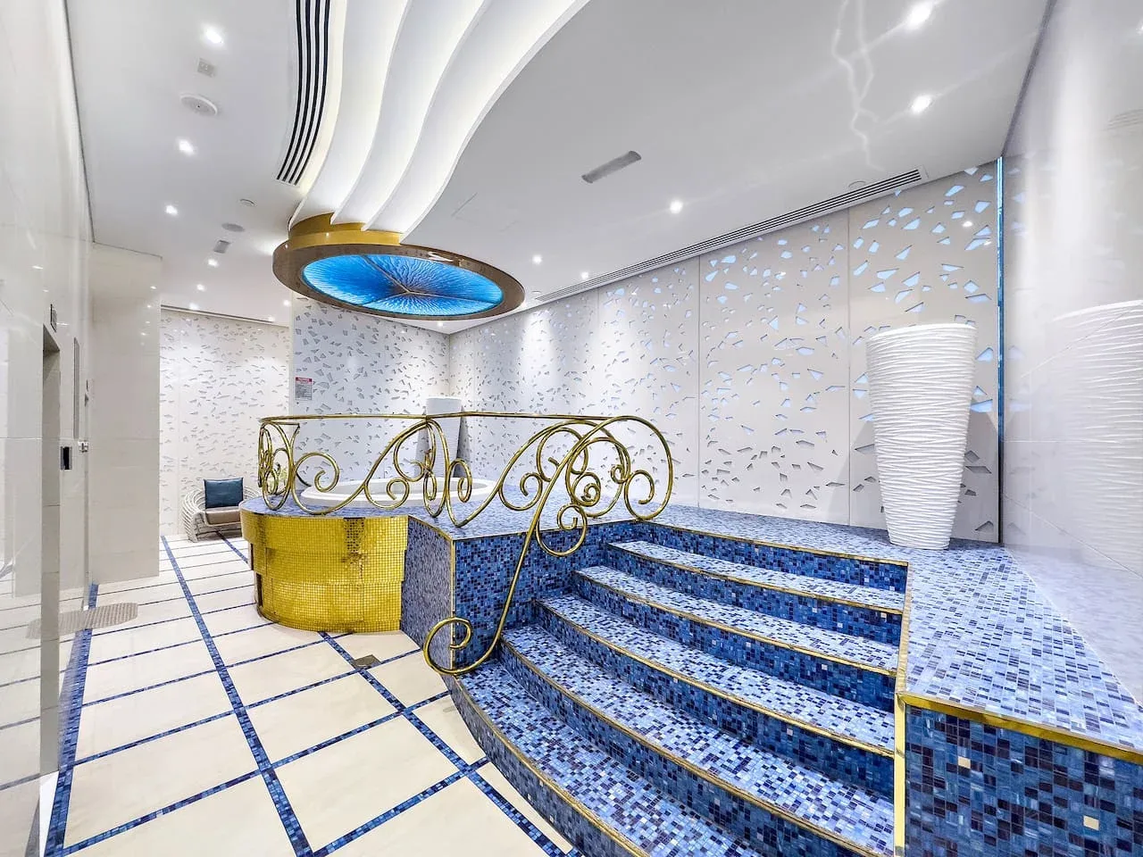 Un interior alicatado presenta escalones de mosaico azul, barandillas decorativas y una lámpara circular en el techo.