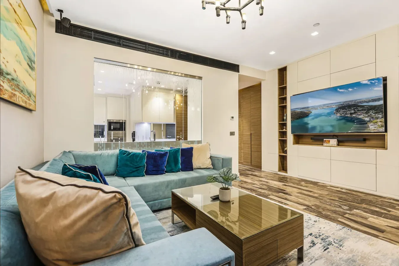 Una sala luminosa con asientos turquesa, una mesa de centro de vidrio y un televisor en la pared.