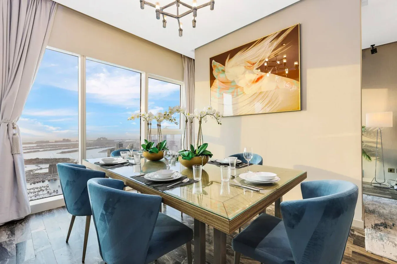 Comedor con una mesa de vidrio y asientos azules junto a grandes ventanales.
