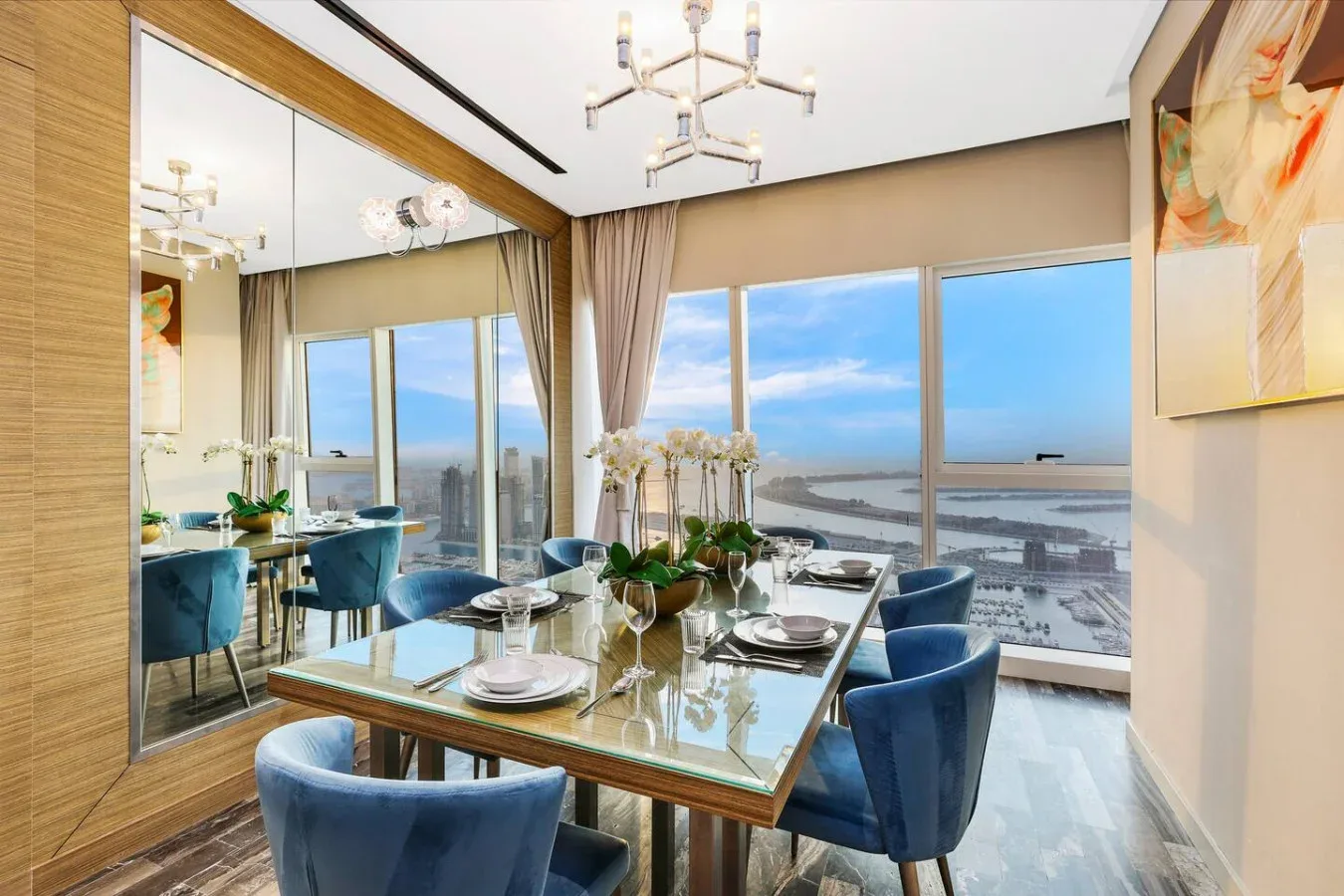 Comedor con mesa de vidrio y asientos azules junto a grandes ventanas con vistas al agua.