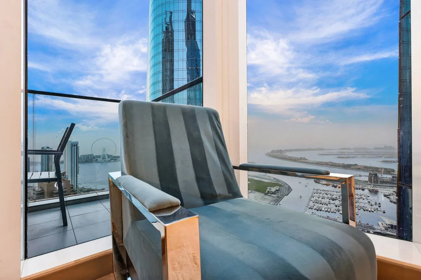 Un sillón acolchado está junto a ventanales con vistas al paseo marítimo.