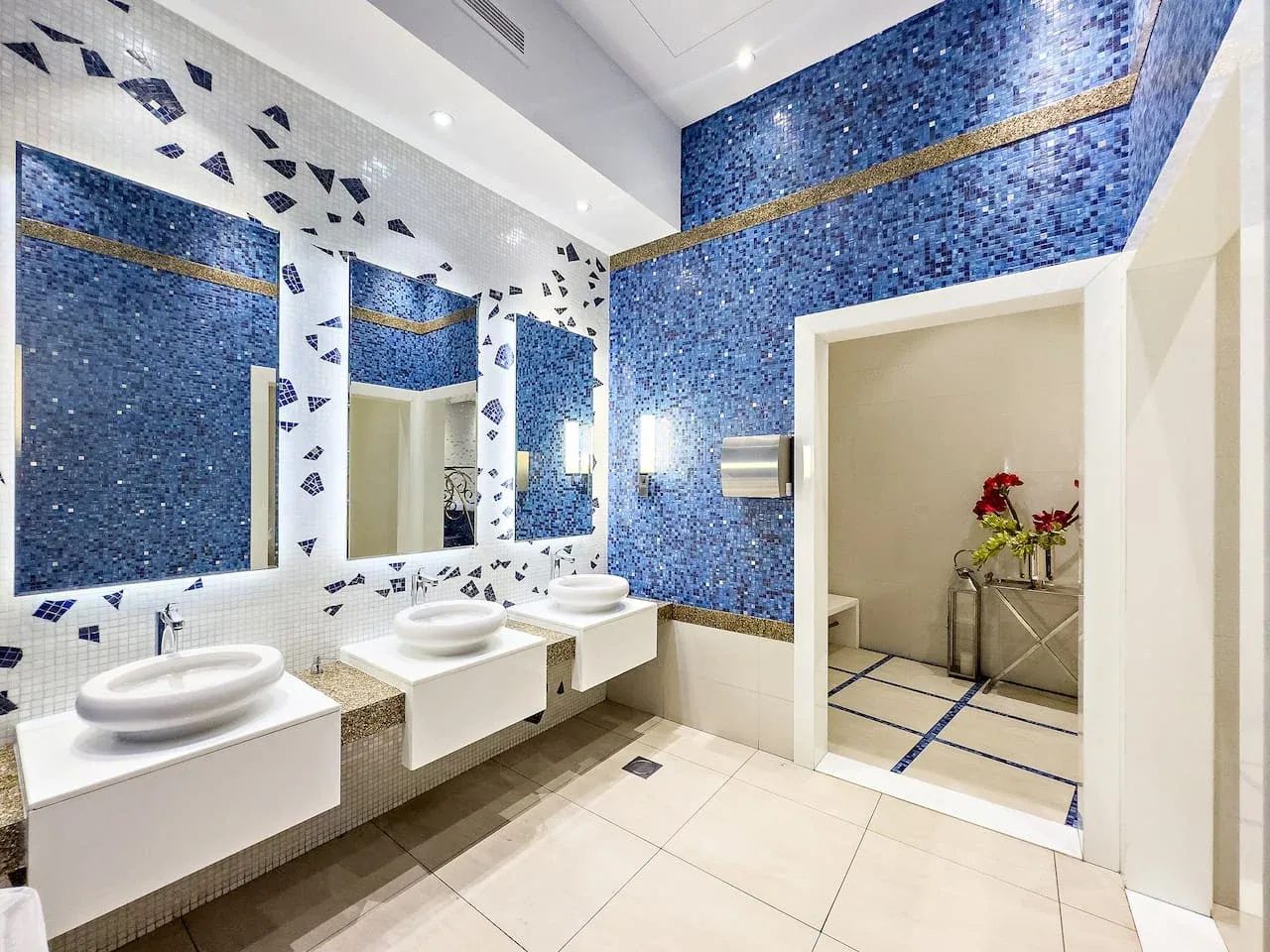 Un baño luminoso con paredes de mosaico azul y lavabos blancos.