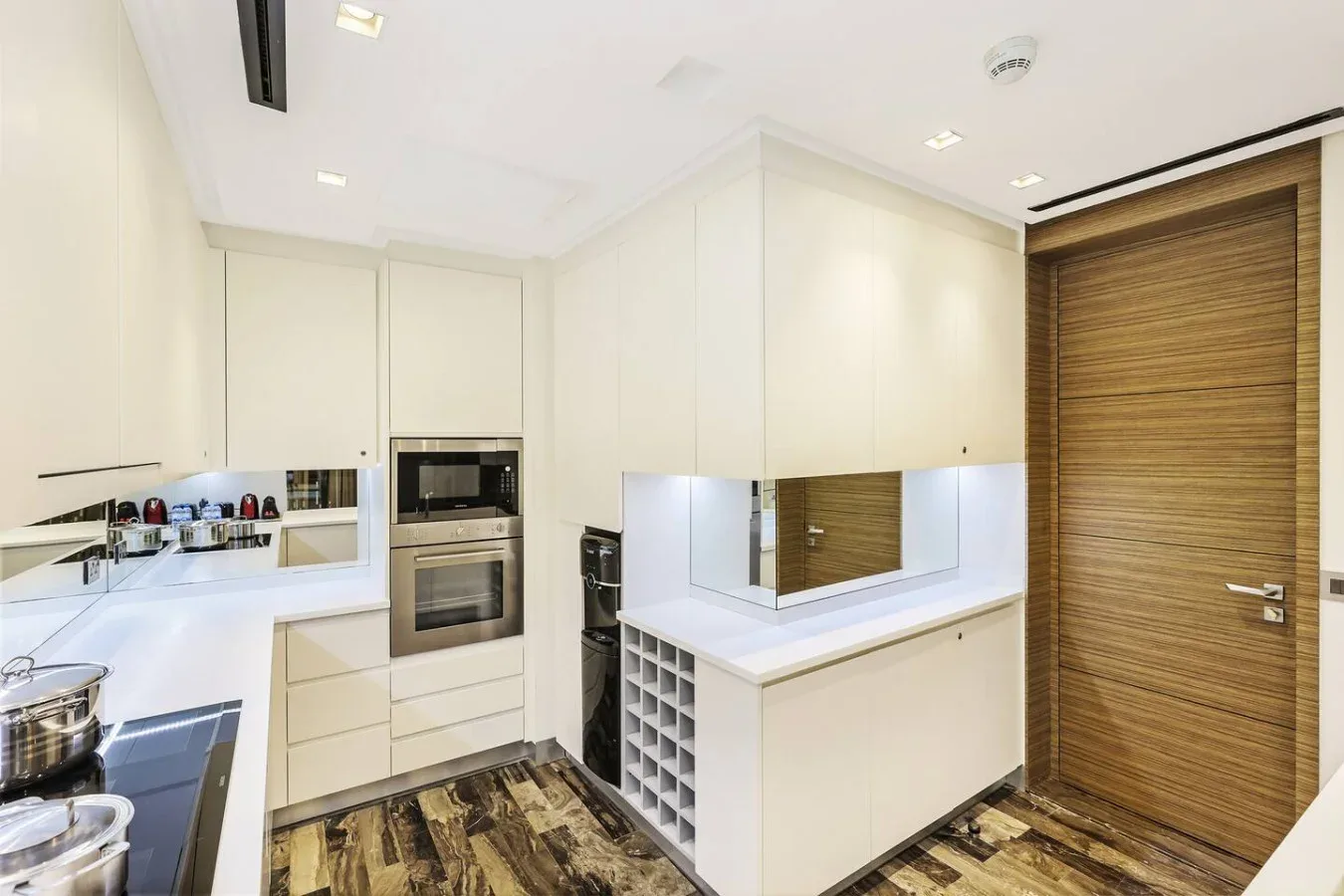 Una cocina luminosa con gabinetes blancos, electrodomésticos empotrados y una puerta de acabado en madera.