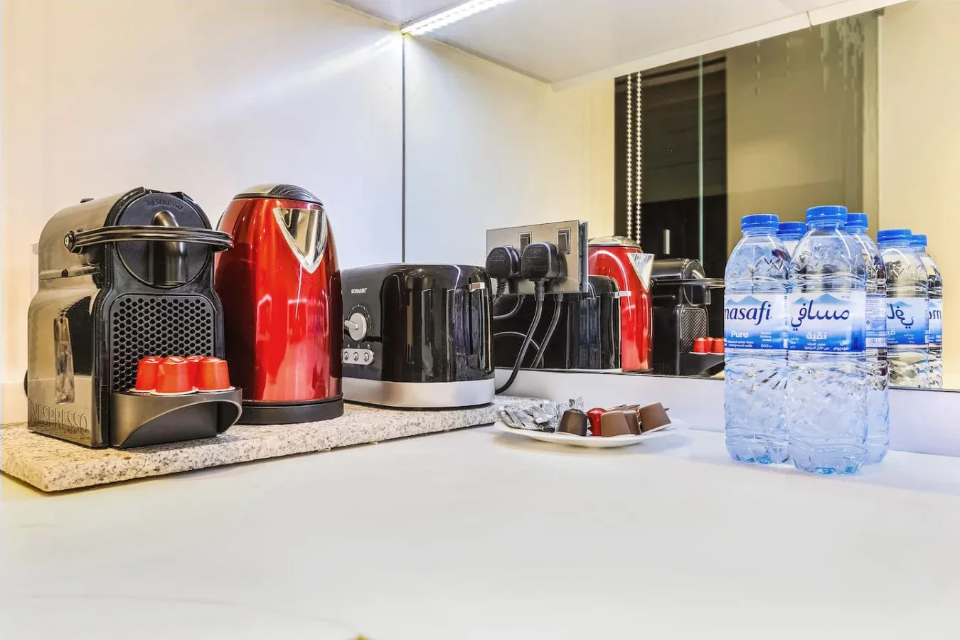 Una estación de café sobre la encimera con cafeteras, tazas y agua embotellada.