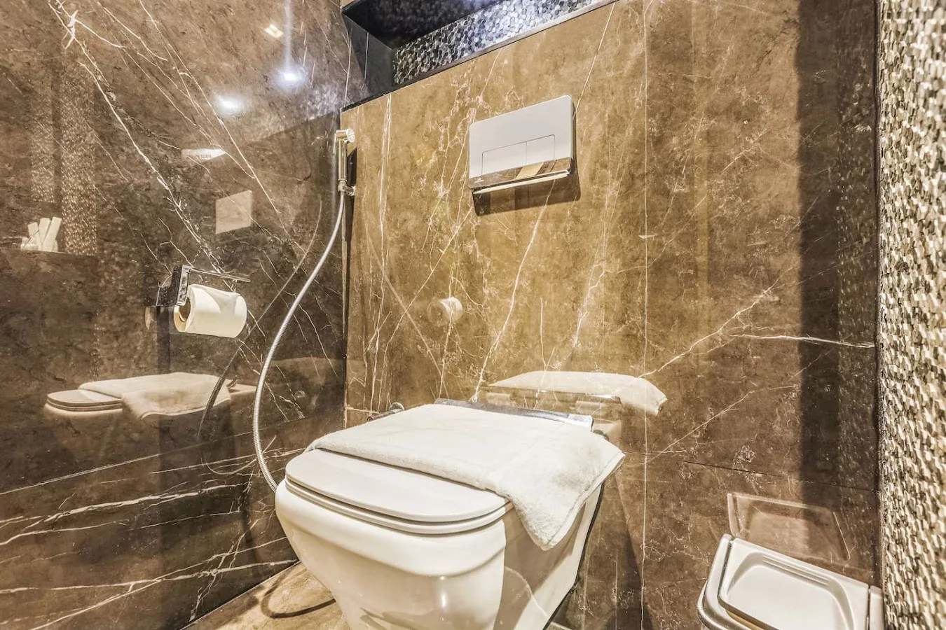 Un baño con inodoro, ducha de mano y paredes marrones con vetas.