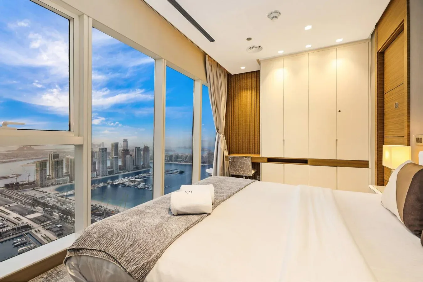 Un dormitorio con una cama bien tendida junto a ventanales con vistas a la ciudad.
