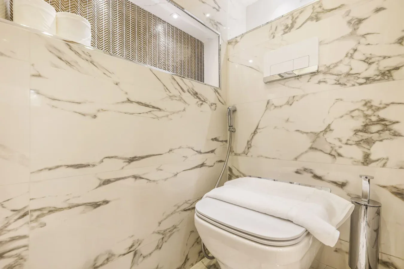 Un baño con inodoro, ducha de mano y paredes con vetas de mármol.