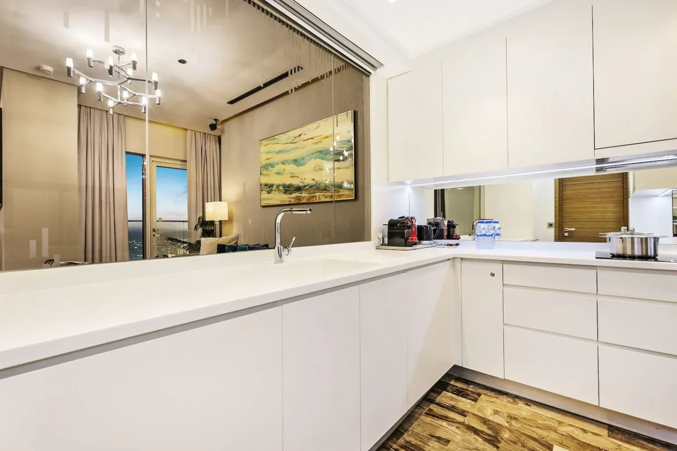Una cocina luminosa con gabinetes blancos, una isla larga y un espejo grande.