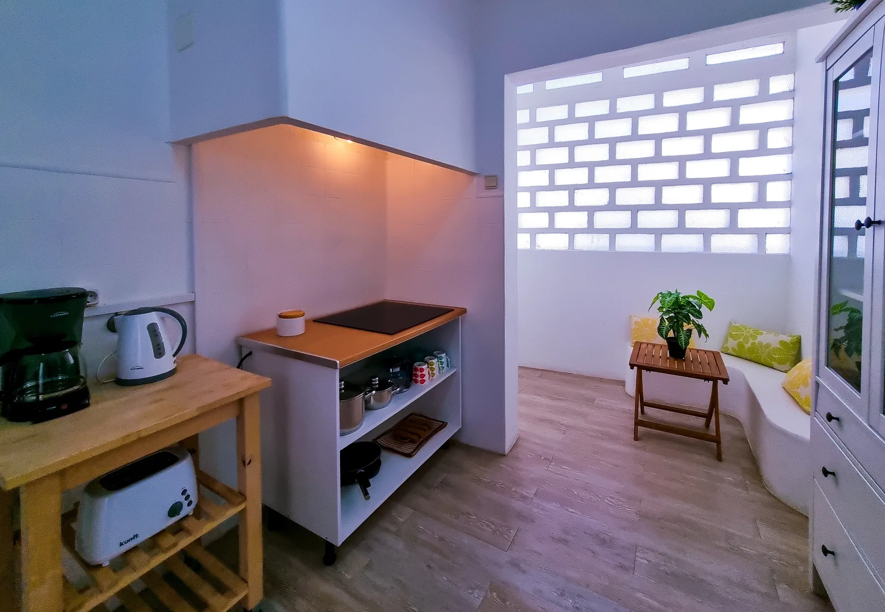 A compact kitchen opens onto a bright seating area with a small table and plant.