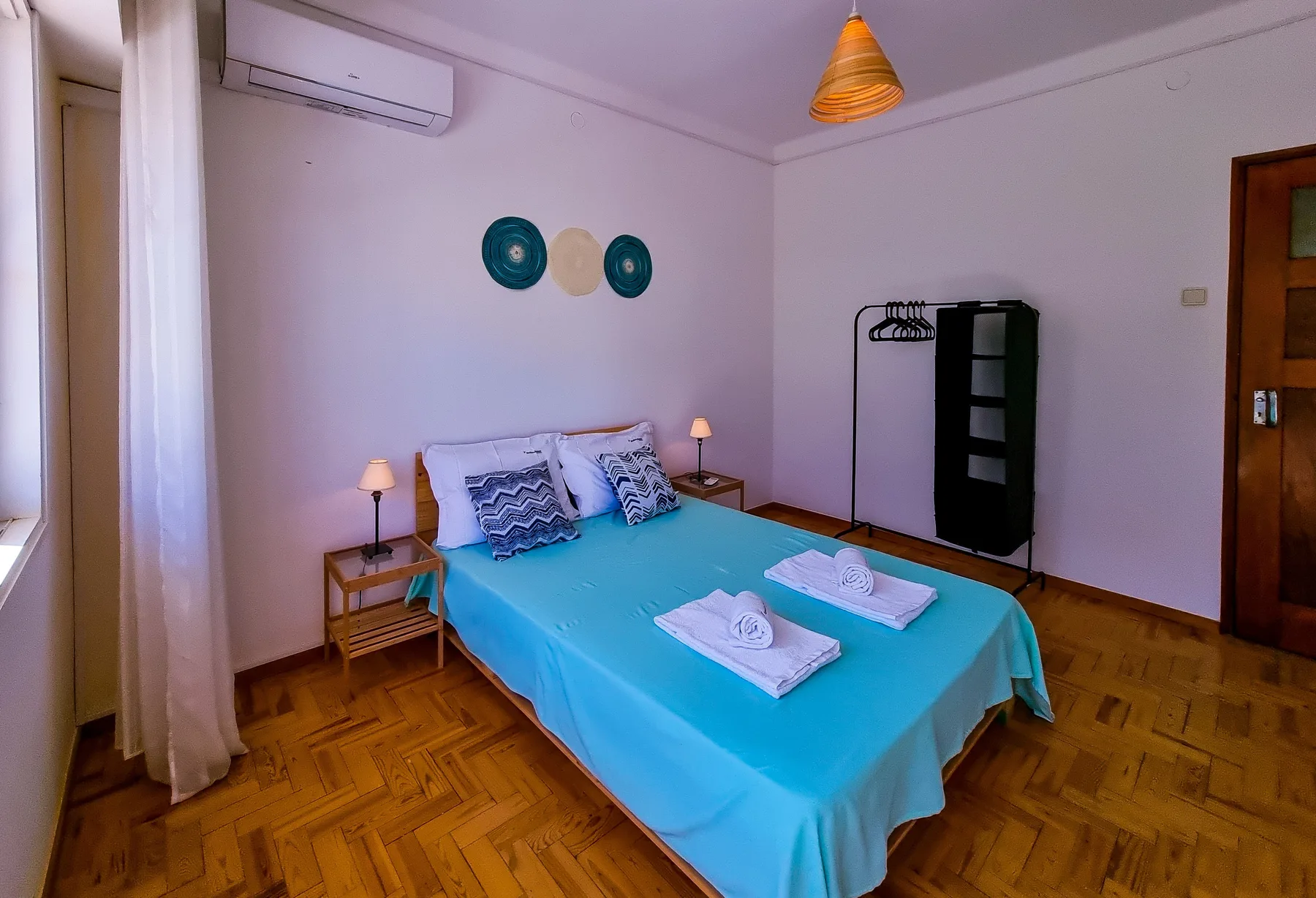 A bedroom with a turquoise bedspread and towels laid out on the bed.