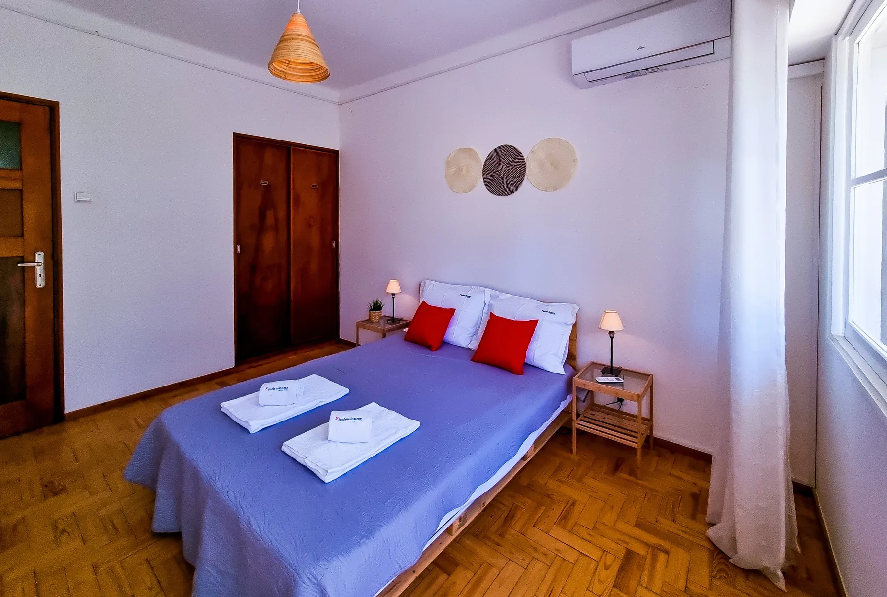 A bedroom with a bed dressed in purple bedding and a large window.