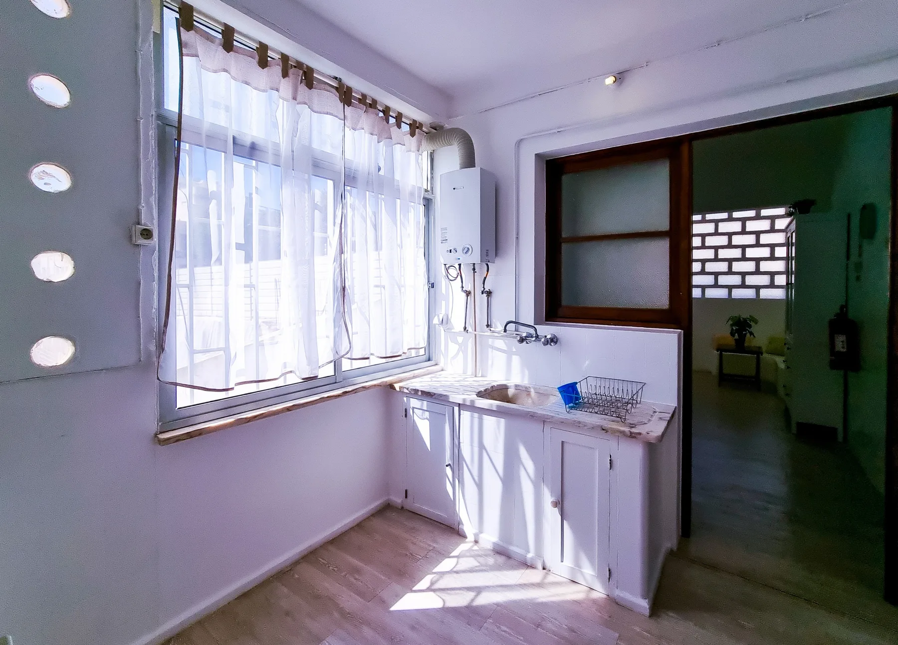 Una cocina luminosa con un fregadero bajo una gran ventana con cortinas.