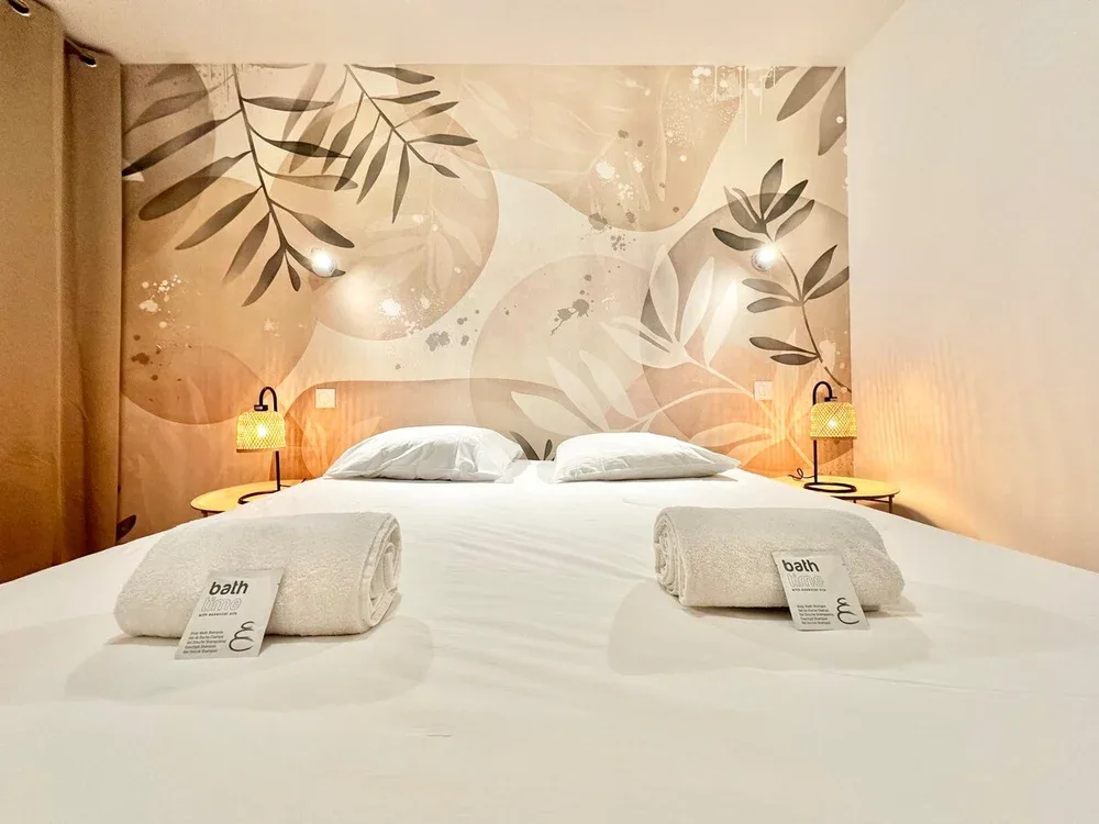A neatly made bed sits against a wall mural of leaves and abstract shapes.
